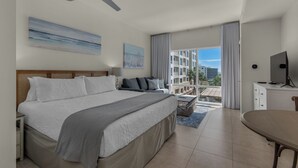 Habitación de hotel con cama, escritorio, silla, televisión y balcón con vistas a edificios.
