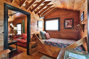 A cozy cabin with a loft bed, a sofa, and a dining area. - The Hayloft - A Sayles Ranch Home (Abilene)