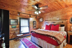 Ein Schlafzimmer einer Holzhütte mit einem Bett, einem Deckenventilator, einem Fenster, einem Stuhl und einem Teppich.