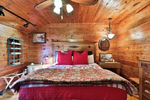 A wooden cabin bedroom with a bed, a nightstand, a lamp, a dresser, and a wall-mounted shelf. - The Hayloft - A Sayles Ranch Home (Abilene)