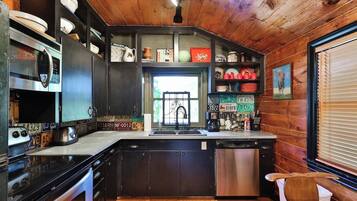 A kitchen with wooden cabinets, a stainless steel dishwasher, and a variety of dishes and kitchenware on shelves.