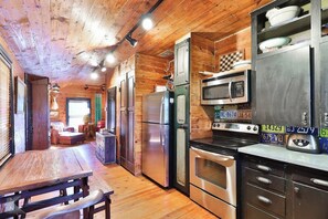 A wooden interior with a kitchen area featuring stainless steel appliances, a dining table, and a bench. - The Hayloft - A Sayles Ranch Home (Abilene)