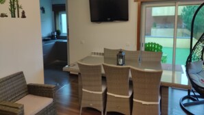 Un coin repas avec une table et des chaises, un téléviseur fixé au mur et une vue sur l’extérieur grâce à une porte-fenêtre coulissante.