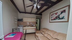 Een knus woongedeelte met een kitchenette, een eethoek met tafel en stoelen, een bank en een plafondventilator.