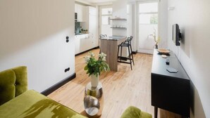 Eine moderne Küche mit weißen Schränken, ein Essbereich mit einem schwarzen Stuhl und ein grünes Sofa.