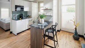 Eine moderne Küche mit weißen Schränken, einer schwarzen Arbeitsplatte und einer zentralen Kochinsel. Auf der Insel stehen zwei schwarze Barhocker und eine Vase mit Blumen.