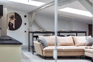 A modern living room with a sofa, a dining table, and a kitchen area.