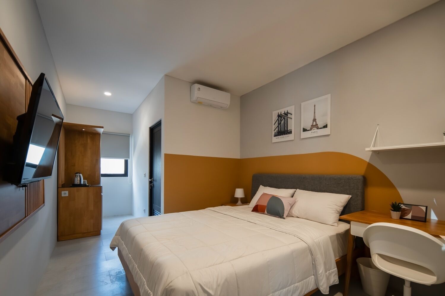 A hotel room with a bed, bedside table, chair, TV, and artwork on the wall.
