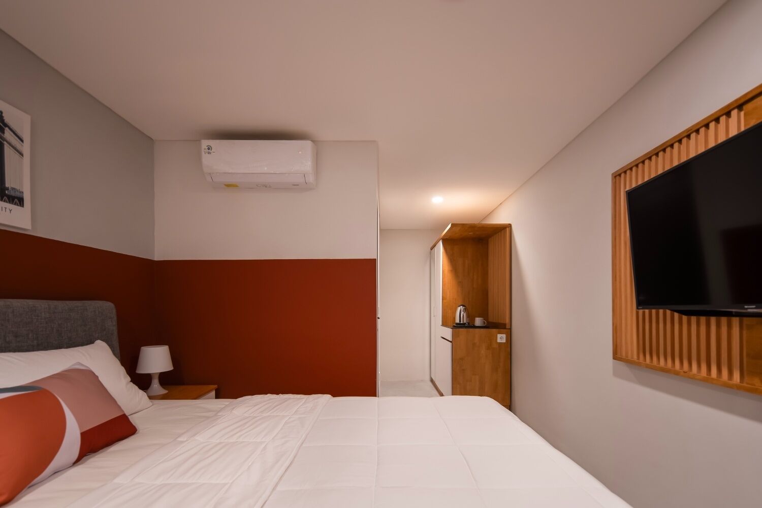 Hotellihuone, jossa on sänky, seinälle asennettu televisio, puinen kaappi ja ovi, joka johtaa kylpyhuoneeseen.