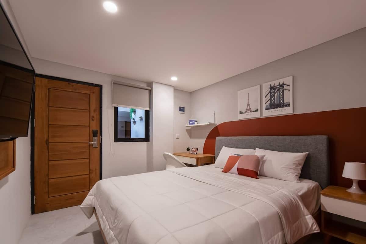 A bedroom with a bed, a wooden wardrobe, a bedside table with a lamp, and a small shelf with decorative items.