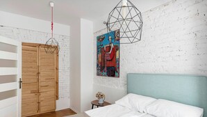 A bedroom with a bed, a wooden wardrobe, a geometric pendant light, a wall-mounted painting, and a small table with a vase. - Roxy by Q4Apartments (Gdynia)