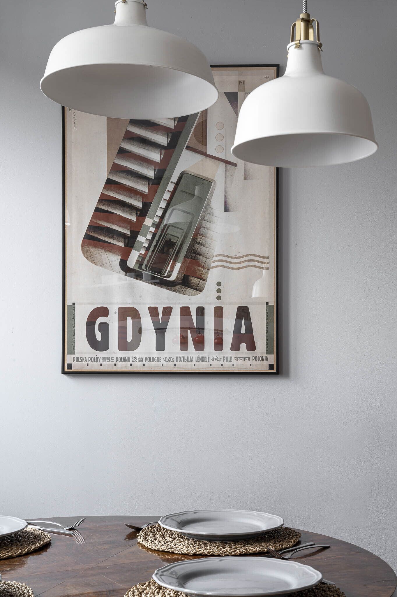 Una mesa de comedor con platos blancos y cubiertos, frente a una pared con un cartel enmarcado.