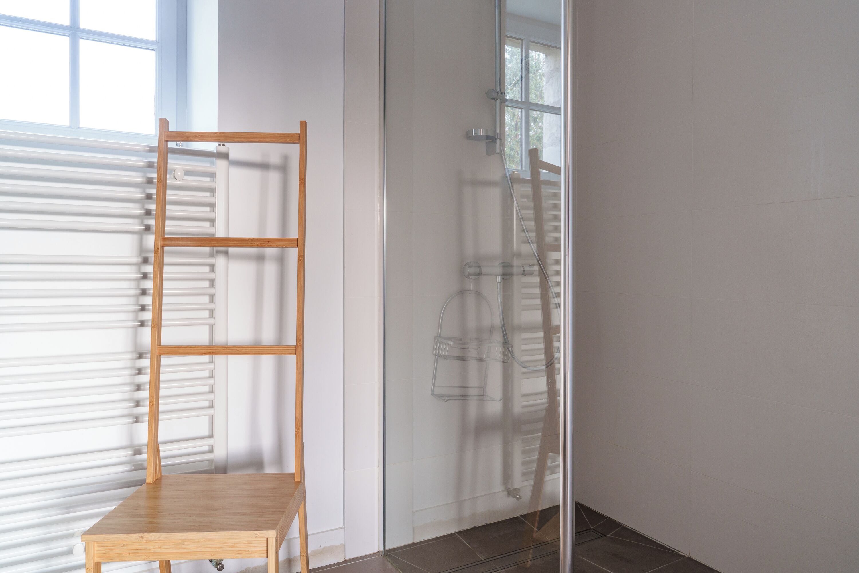 Ein Zimmer mit einem Holzsessel, einem Heizkörper und einer Duschkabine aus Glas.