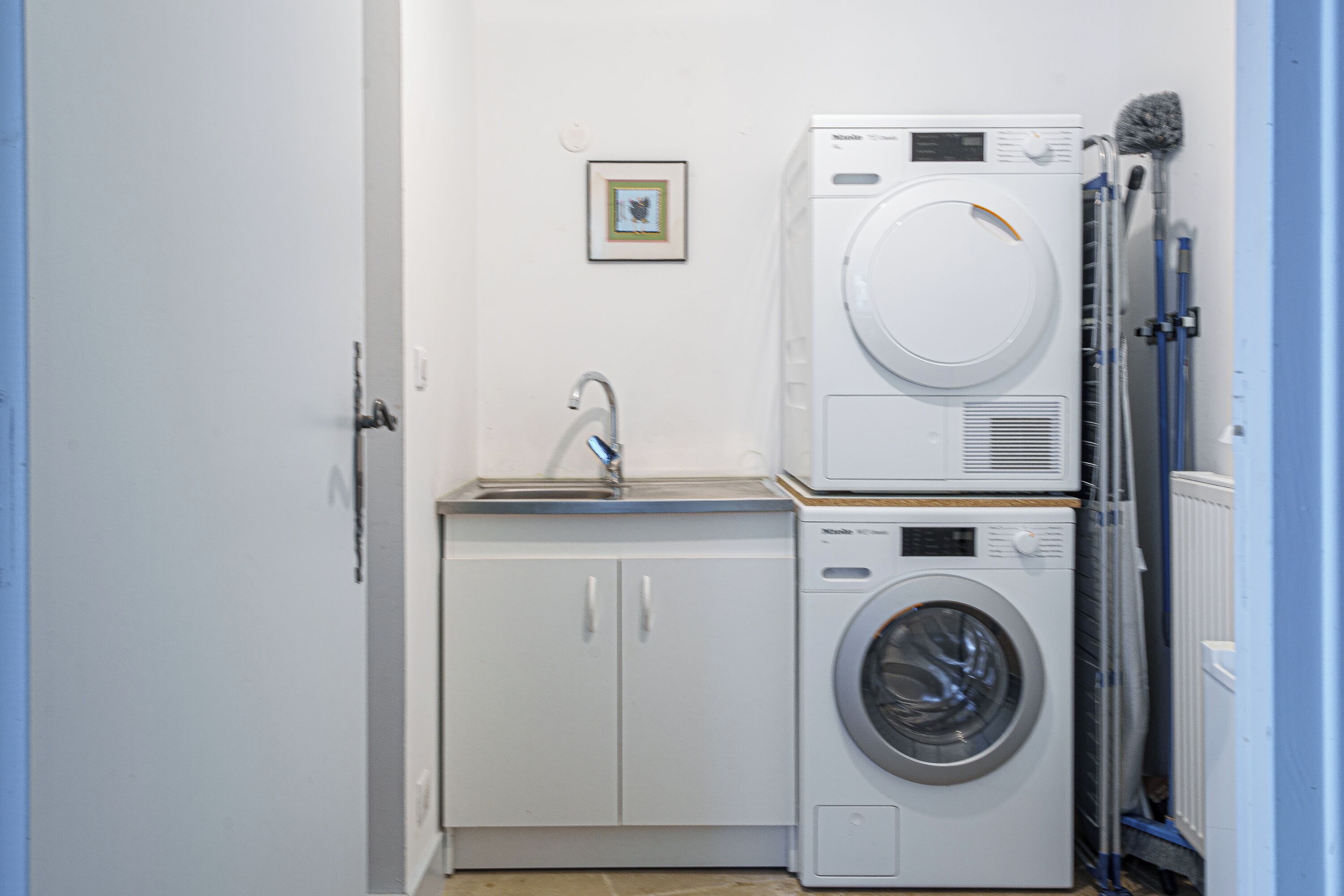 A laundry area with stacked washers and dryers, a sink, and a framed picture on the wall.