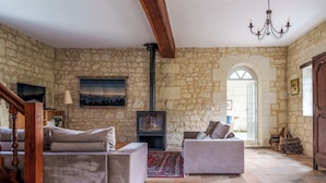 Un salon aux murs de pierre, doté de deux canapés, d’une cheminée et d’un lustre.