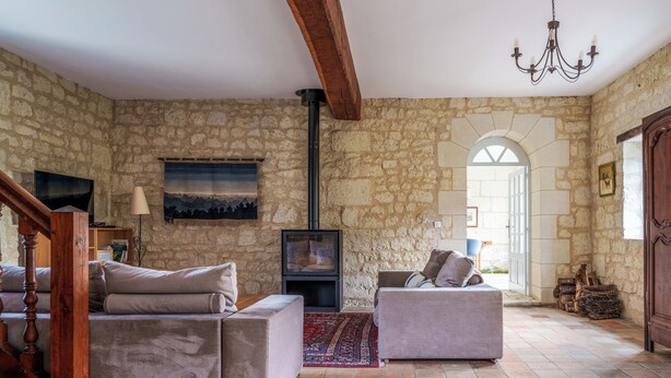 A stone-walled living room with two sofas, a fireplace, and a chandelier.