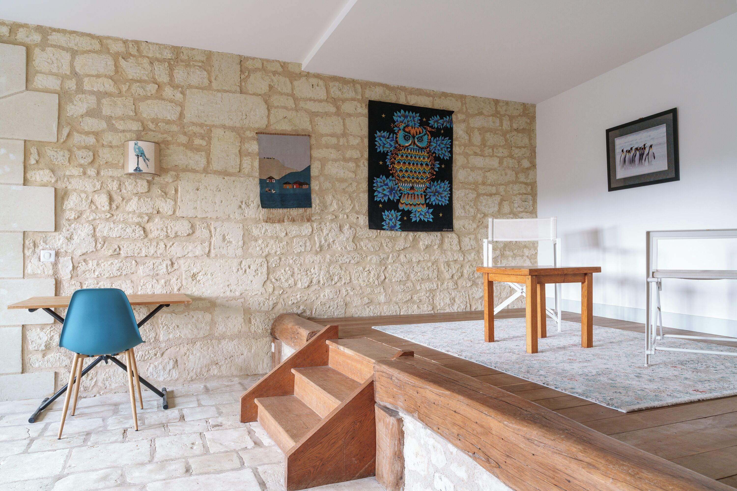 A room with a stone wall, a wooden bench, a blue chair, and a wooden table.