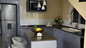 Une cuisine compacte équipée d’un réfrigérateur, d’un four à micro-ondes et d’une cuisinière. On y trouve un petit îlot central avec un panier de fruits et un grille-pain. La cuisine est dotée de meubles de couleur bleu clair et d’un plan de travail blanc.