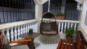 Un balcon accueillant avec un fauteuil suspendu, une table en bois et des plantes en pot.