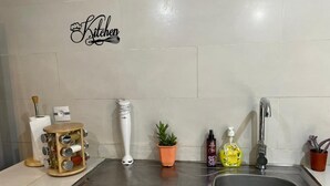 Una cocina con un lavamanos de acero inoxidable, una planta en maceta y un cartel decorativo en la pared.