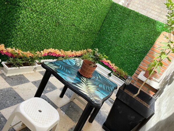 A patio area with a glass table, a white stool, and potted plants.
