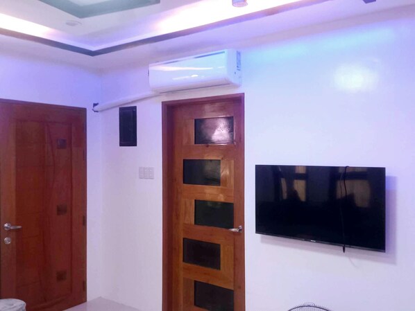 A room with a wooden door, a wall-mounted TV, and an air conditioning unit.