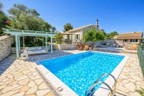 A swimming pool with a stone deck, a covered seating area, and a stone house with a tiled roof. - Villa Agathi - Two Bedroom Villa, Sleeps 4 (Paxi)