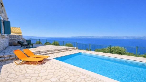 A swimming pool with stone flooring, two orange lounge chairs, a stone wall, and a view of the sea. - Villa Agathi - Two Bedroom Villa, Sleeps 4 (Paxi)