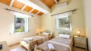 A bedroom with two beds, wooden ceiling beams, and windows with curtains. - Villa Agathi - Two Bedroom Villa, Sleeps 4 (Paxi)