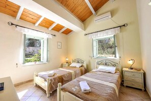 A bedroom with two beds, wooden ceiling beams, and windows with curtains. - Villa Agathi - Two Bedroom Villa, Sleeps 4 (Paxi)