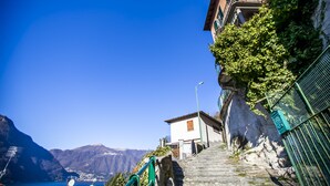 A narrow staircase leading up to a building with a view of mountains and a lake. - Le Titino (Nesso)