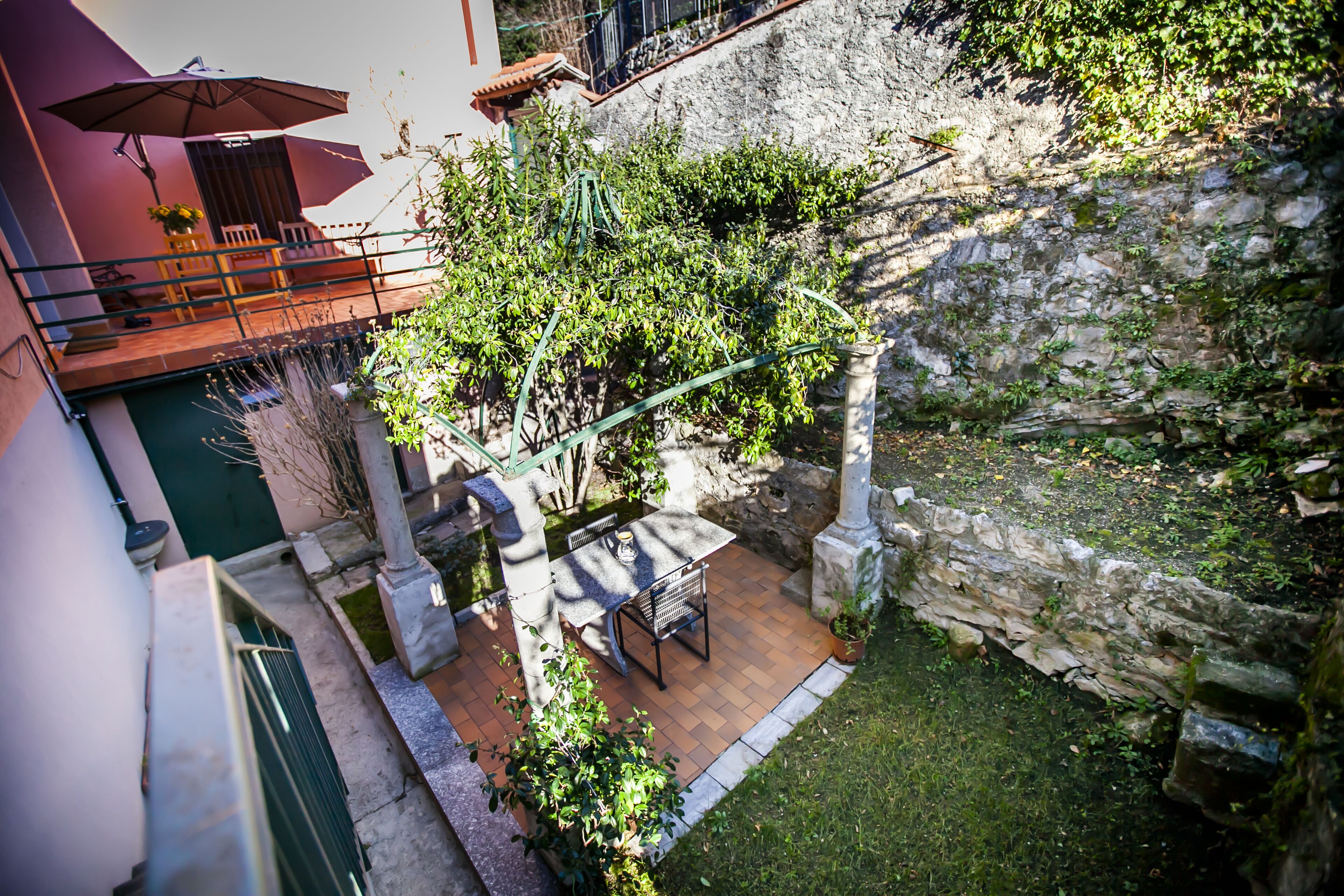 A courtyard with a table and chairs, surrounded by greenery and stone walls.
