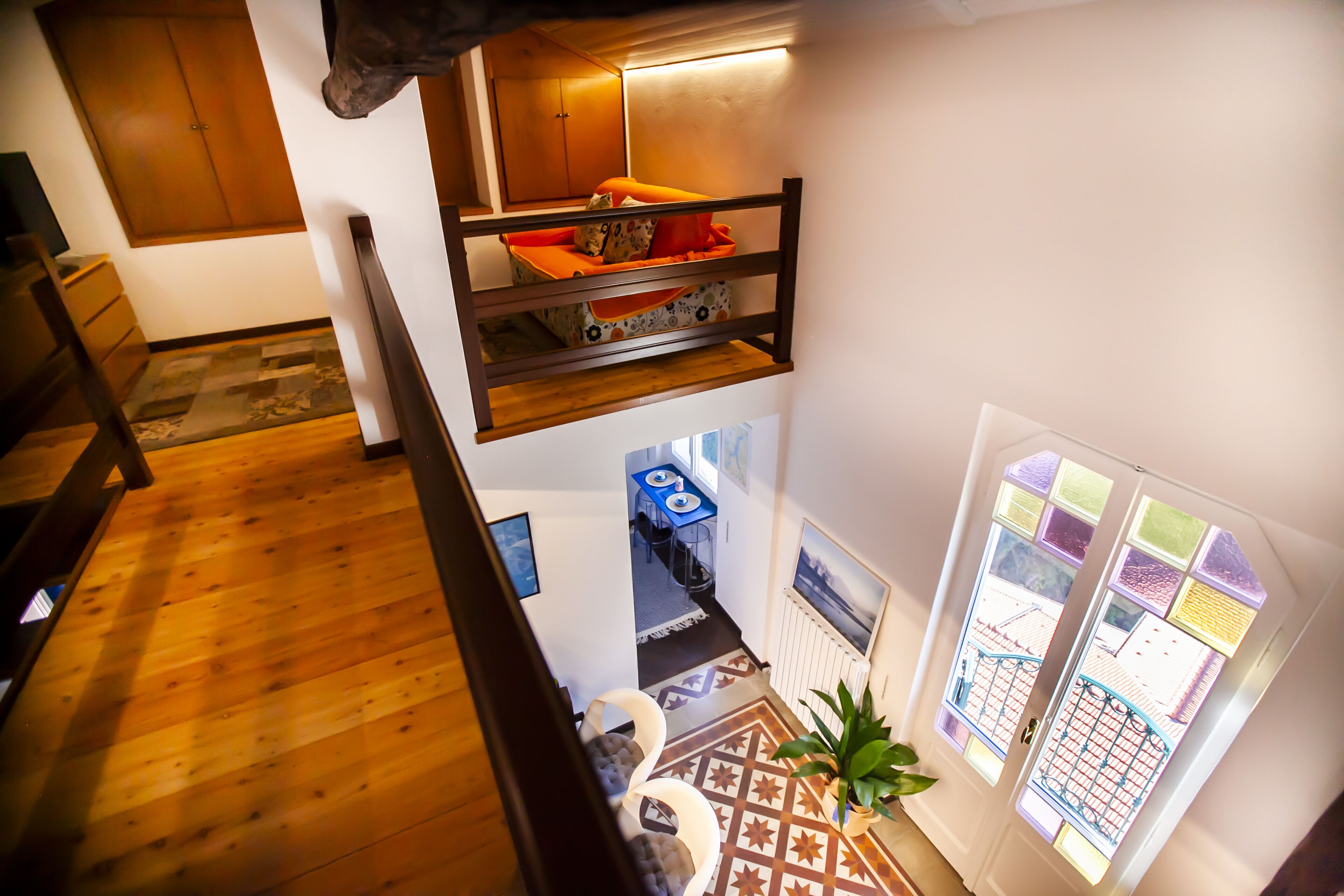 Een meerlaags interieur met een houten trap, een stapelbed, een eethoek en uitzicht door een raam met glas-in-lood.