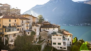 A coastal town with buildings overlooking a body of water and mountains in the background. - Le Titino (Nesso)