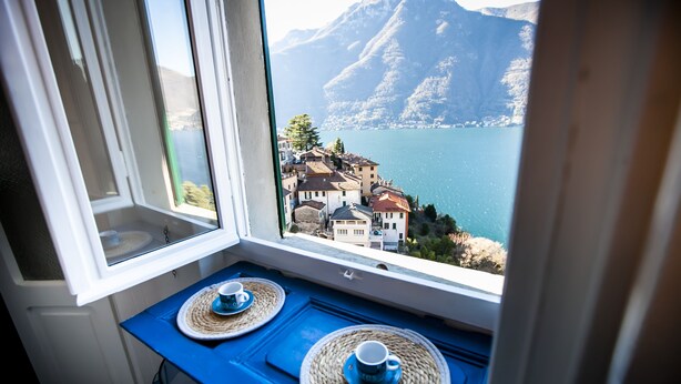 A window view of a lake with buildings and mountains. - Le Titino (Nesso)