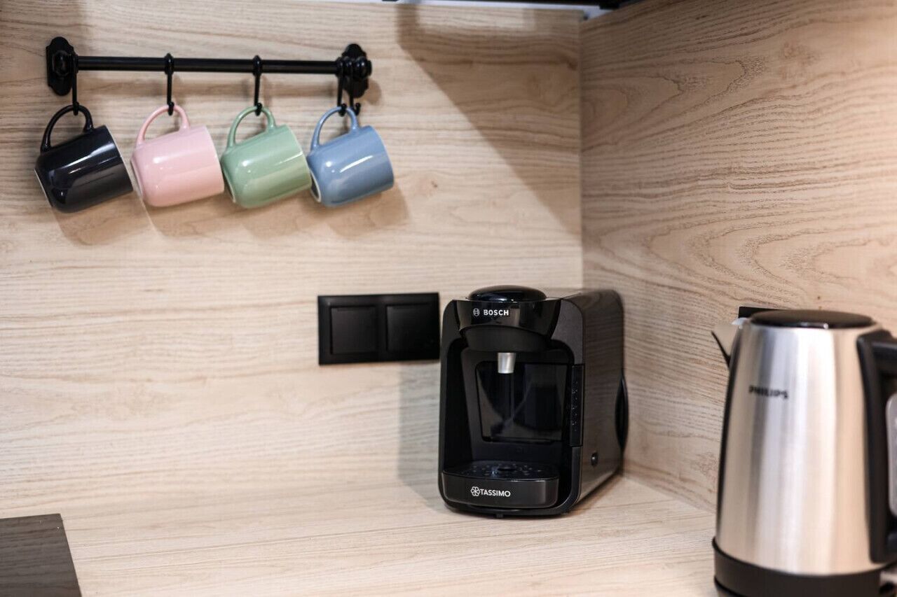 A kitchen with a coffee maker, a kettle, and mugs on a rack.