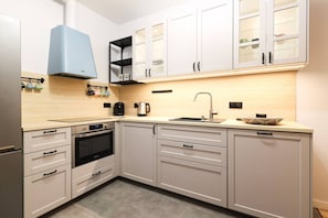 A modern kitchen with white cabinets, a built-in oven, a coffee maker, and a kettle.