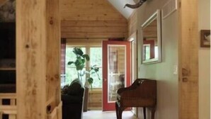 A wooden interior hallway with a red carpet, a piano, and a mirror on the wall. - Spacious Family Cabin, Hot Tub & Pet Friendly! (Cobourg)