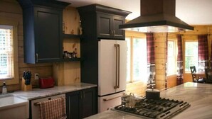 A kitchen with dark cabinets, a white refrigerator, and a central island with a stove. - Spacious Family Cabin, Hot Tub & Pet Friendly! (Cobourg)