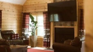 A cozy living room with a fireplace, wooden walls, and a large flat-screen TV. - Spacious Family Cabin, Hot Tub & Pet Friendly! (Cobourg)