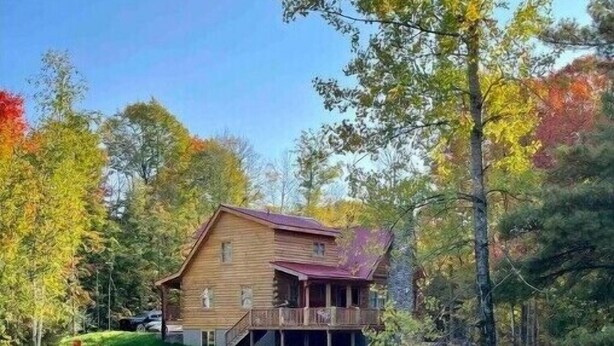 A wooden cabin with a porch, surrounded by autumn foliage and a small stream. - Spacious Family Cabin, Hot Tub & Pet Friendly! (Cobourg)