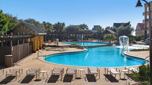 Un espace piscine aménagé dans un complexe hôtelier, avec de nombreux chaises longues et une fontaine.