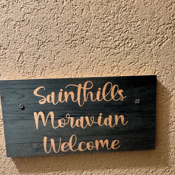 A wooden sign with the text "Saints Hills Moravian Welcome" mounted on a textured wall.