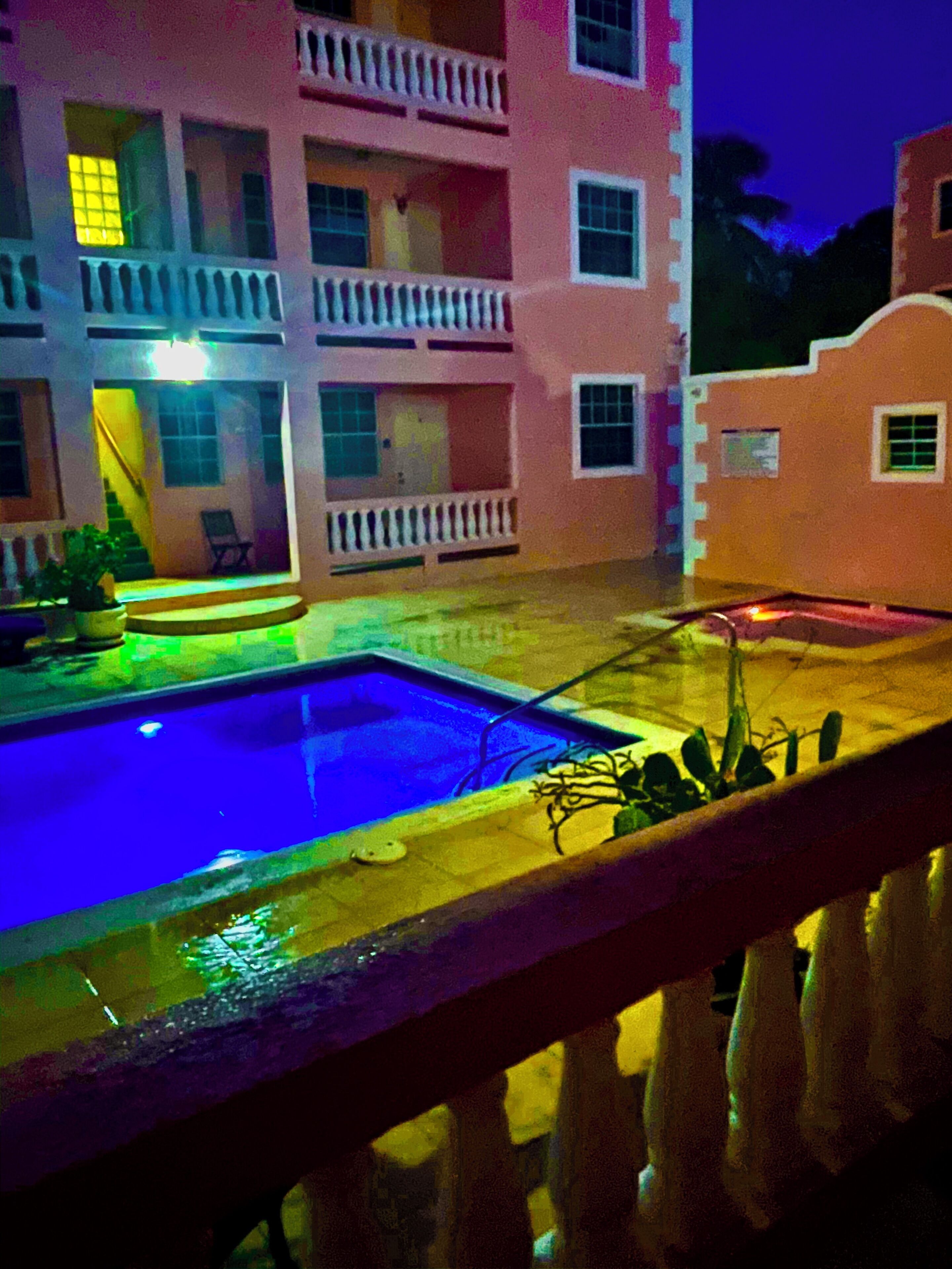 A hotel with a swimming pool, balconies, and a staircase leading to the entrance.