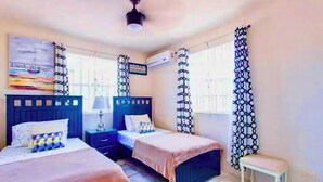 A bedroom with two beds, a nightstand, a bench, and a painting on the wall.