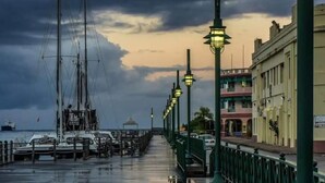 A waterfront promenade with a row of street lamps, a pier with boats, and buildings along the side.