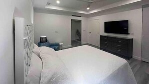 Une chambre à coucher moderne avec un grand lit, un téléviseur fixé au mur et une commode.