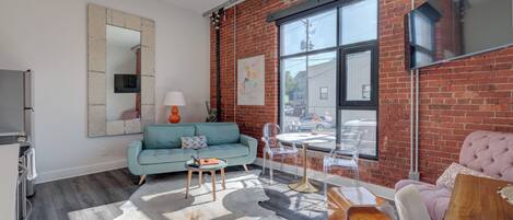 A modern living room with a brick wall, a large window, a sofa, a coffee table, and a TV.
