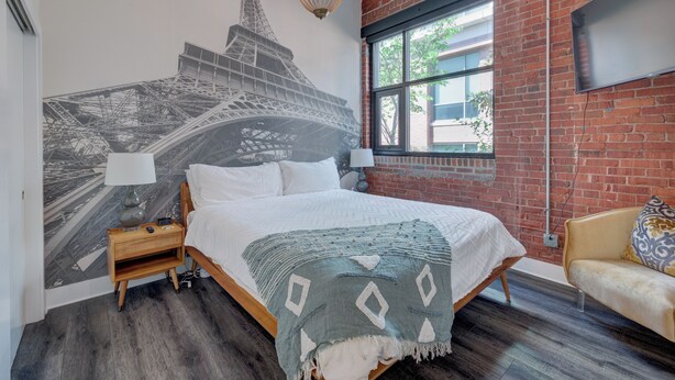 Un dormitorio con una cama grande, una mesita de noche, una l ámpara, un sofá y un mural de la Torre Eiffel.