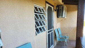 A balcony with two blue chairs, a window with a metal grill, and an air conditioning unit on the wall. - Sea View 3 Bedroom Apartment in St. Thomas

 (St Thomas)